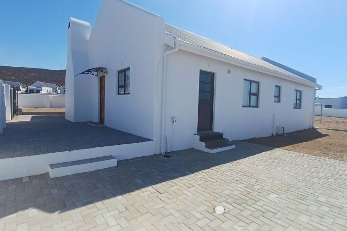A view of the rear exterior of the house, featuring paved patio areas, white rendered walls, and a metal roof.