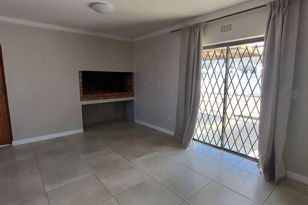 A spacious living area featuring large floor tiles, a built-in brick fireplace, and sliding glass doors with security gates leading to the exterior.