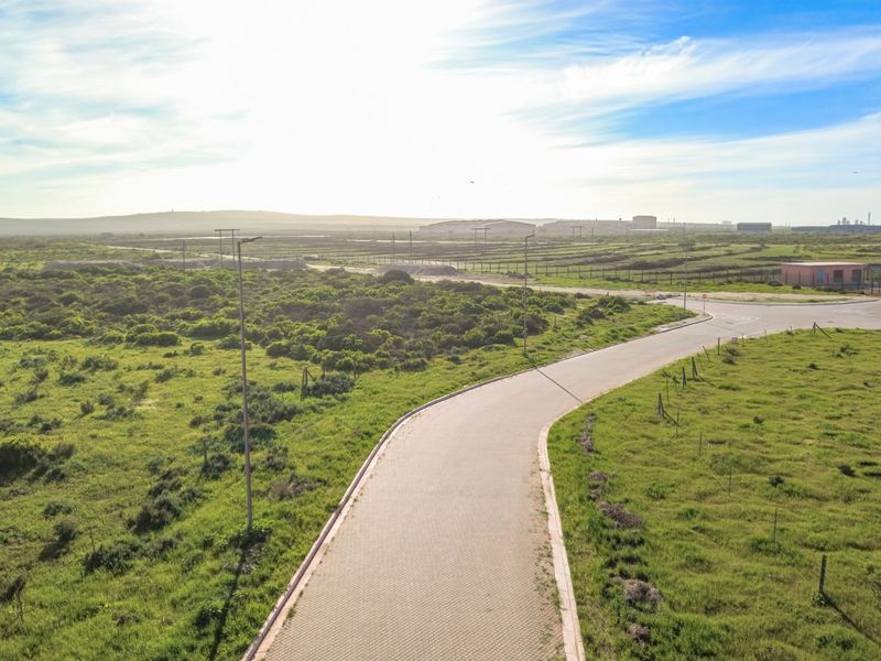 An aerial view of a paved access road leading through an open industrial landscape with surrounding vegetation and perimeter fencing.