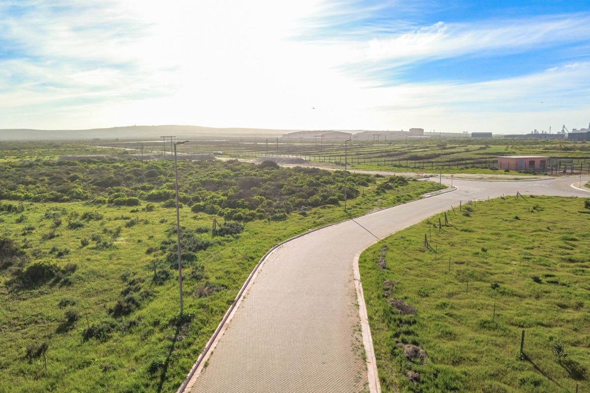 An aerial view of a paved access road leading through an open industrial landscape with surrounding vegetation and perimeter fencing.