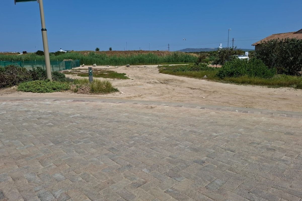 A view of a vacant residential plot from the street, featuring paved road access and natural vegetation.