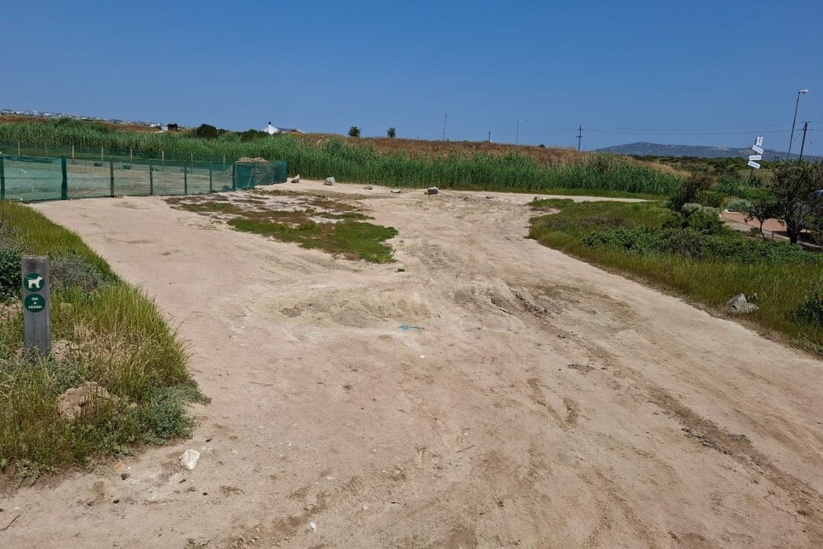 A view of a vacant residential plot featuring sandy terrain, natural vegetation, and perimeter fencing.