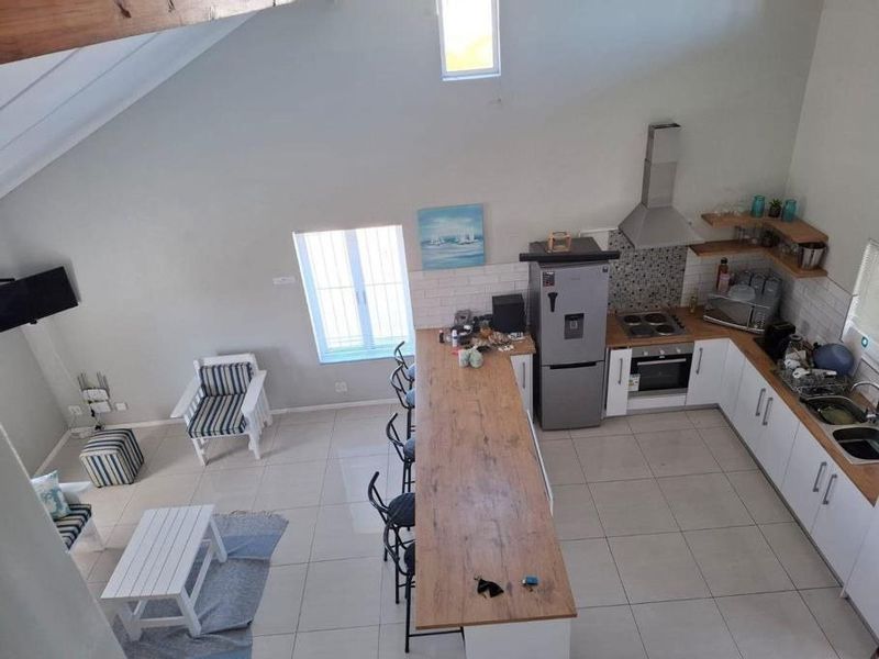 Spacious open-plan living and kitchen area featuring vaulted ceilings, exposed timber beams, a central island, and modern tiled flooring throughout.
