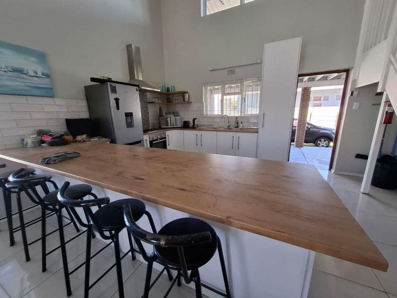 Open-plan kitchen featuring a large breakfast bar, modern cabinetry, tiled backsplash, and high ceilings, creating a bright and functional living space.