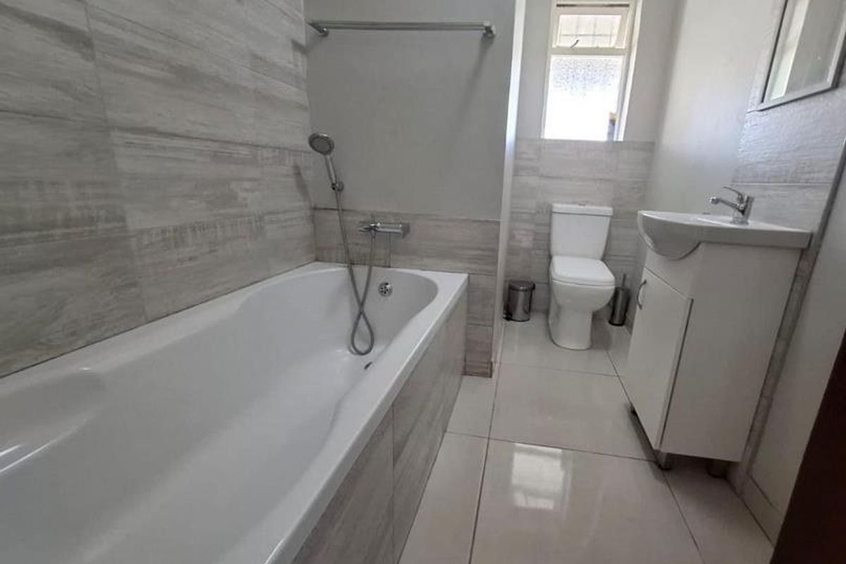 A modern, clean bathroom featuring a bathtub with handheld shower, a vanity basin, and a toilet, finished with neutral wall and floor tiling.