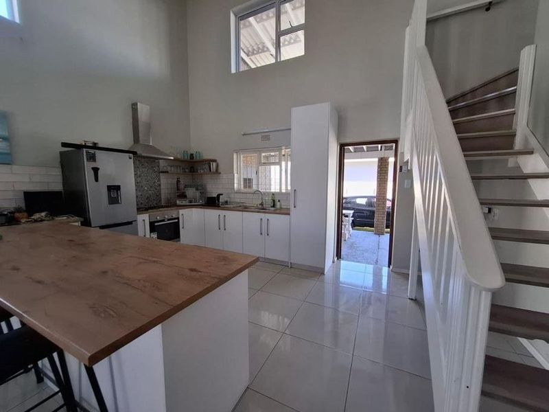 Open-plan kitchen featuring modern cabinetry, a central island, and tiled flooring, with an adjacent staircase leading to the upper level.