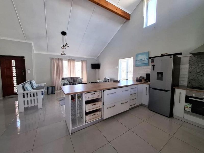 Spacious open-plan living area featuring a vaulted ceiling with exposed timber beam, modern kitchen island, and tiled flooring throughout.