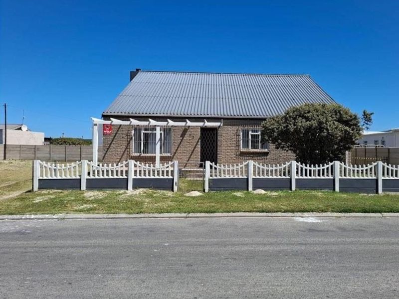 Front view of a single-story brick house featuring a corrugated metal roof, a front pergola, and a secure perimeter fence.
