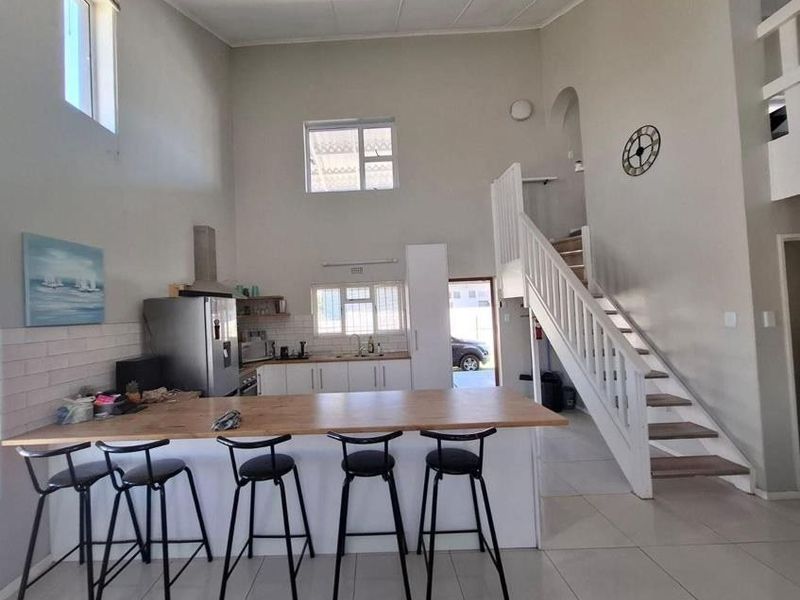 Open-plan living area featuring a kitchen with island, double volume ceilings, and a staircase leading to the upper level.