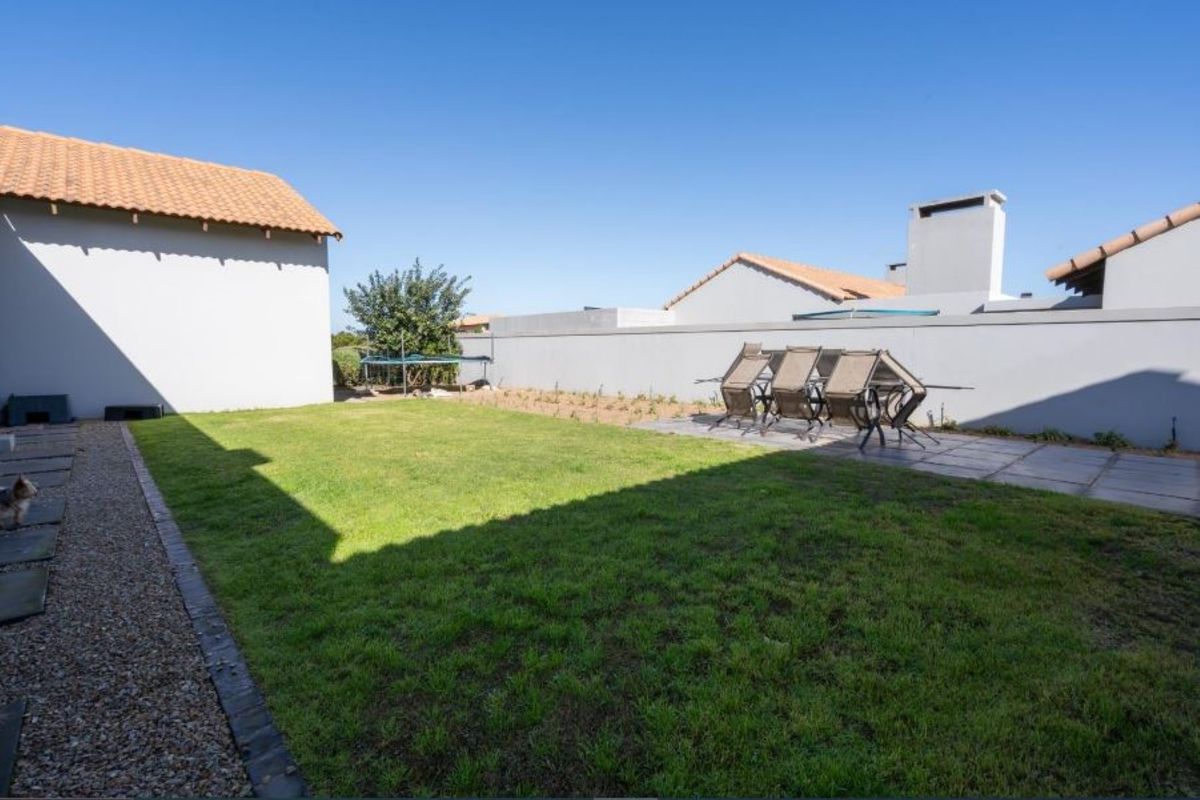A private rear garden featuring a manicured lawn, paved patio area, and perimeter boundary walls.