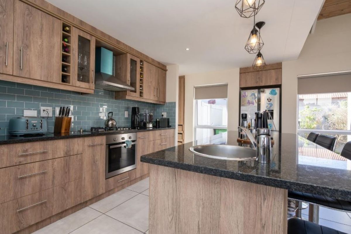 Modern kitchen featuring wood-look cabinetry, granite countertops, a central island with a prep sink, and a stylish blue subway tile backsplash.