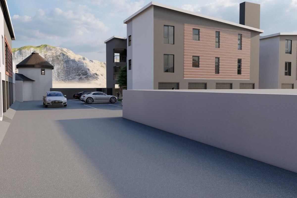 A modern multi-story apartment complex exterior featuring a paved parking area, concrete boundary walls, and integrated garage access.