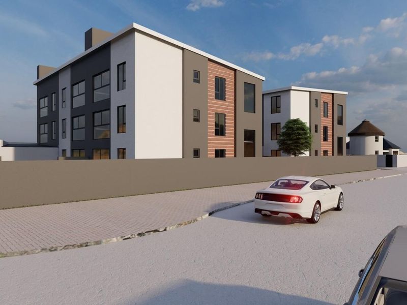 A modern multi-story apartment complex featuring contemporary architectural design, clean lines, and a secure perimeter wall, viewed from the street.