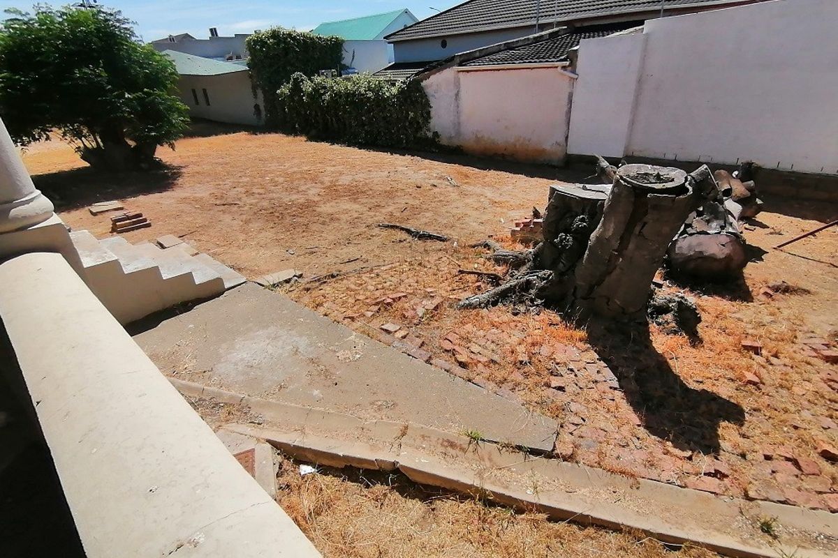 A rear garden area featuring concrete steps leading from the house, a large tree stump, and a dry, unmaintained lawn with boundary walls.