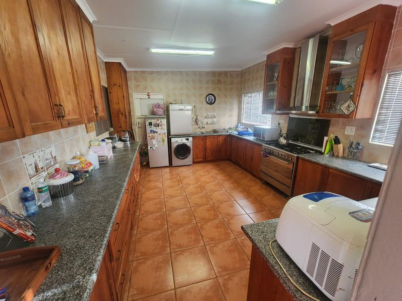 Spacious kitchen featuring extensive wooden cabinetry, granite countertops, tiled flooring, and a stainless steel gas stove with extractor fan.