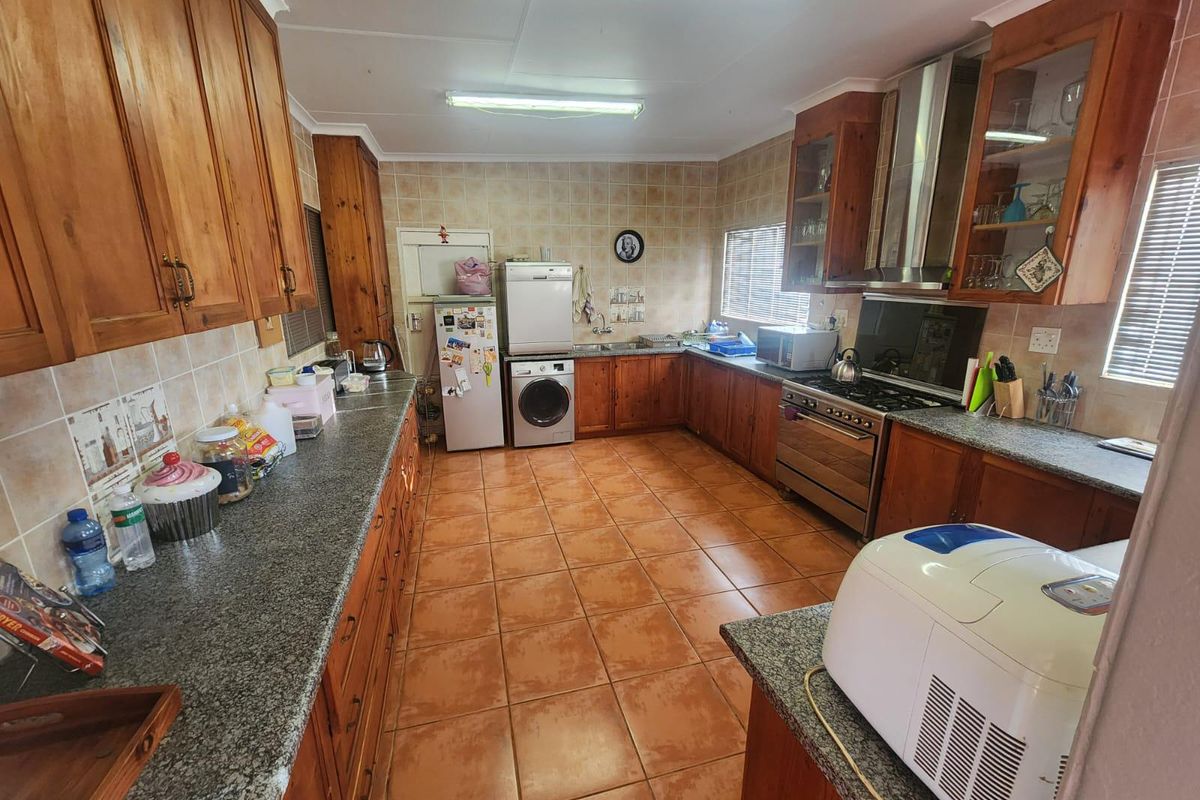 Spacious kitchen featuring extensive wooden cabinetry, granite countertops, tiled flooring, and a stainless steel gas stove with extractor fan.