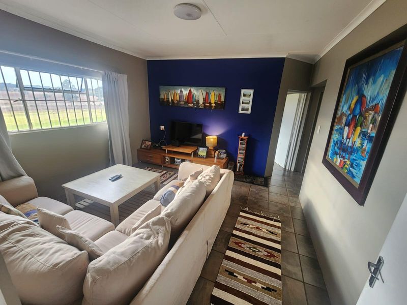 A comfortable living room featuring tiled flooring, a bold blue accent wall, and natural light through a window fitted with security bars.