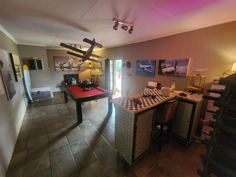 A spacious living area featuring tiled flooring and track lighting, currently utilized as a recreational space with direct access to the outdoors.