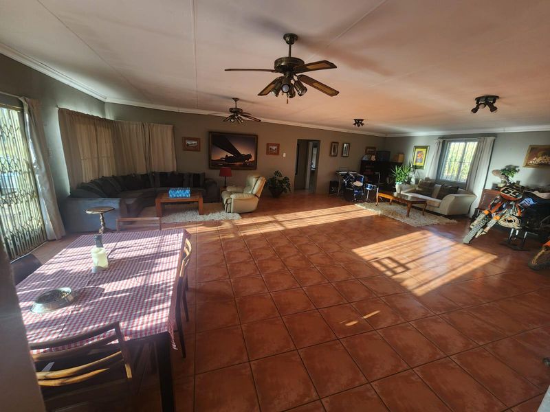 Spacious open-plan living and dining area featuring large format floor tiles, multiple ceiling fans, and natural light through large windows.