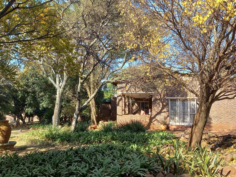 A view of the rear brick facade of the house, featuring a covered patio area and a mature, landscaped garden with established trees.