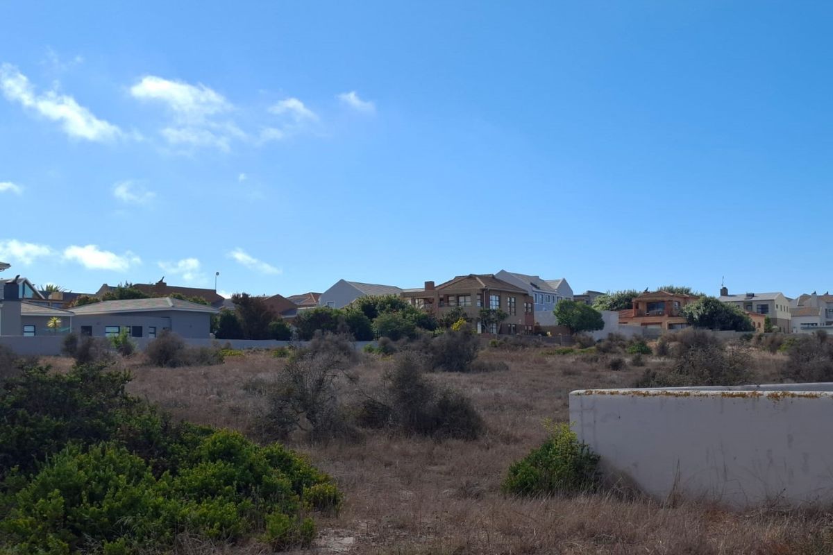 A view of a vacant residential plot featuring natural vegetation and a partial boundary wall, situated within an established neighborhood.