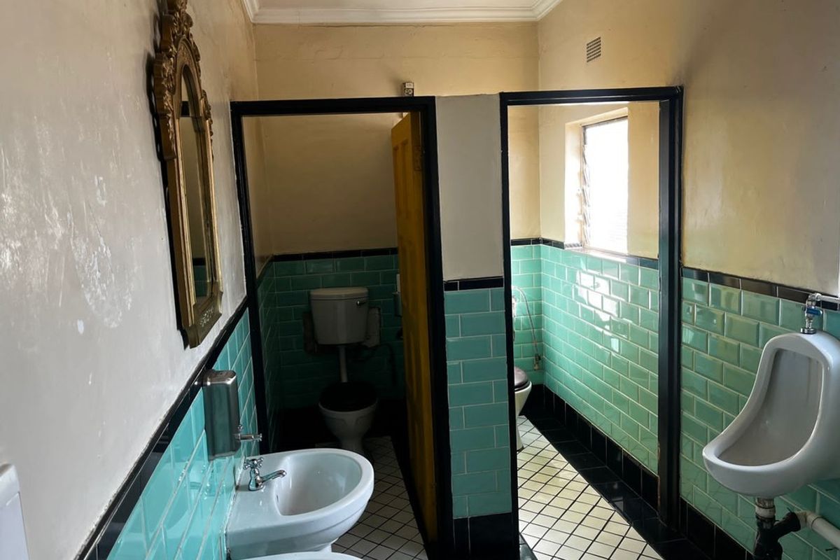 Commercial restroom facility featuring vintage green subway tiling, dual basins, a wall-mounted urinal, and separate toilet cubicles with tiled flooring.