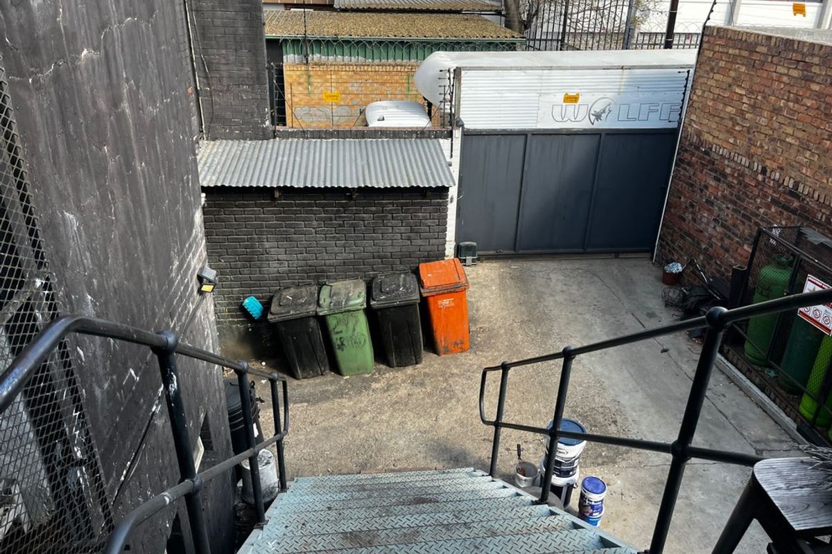 An exterior rear service yard featuring a metal staircase, brick boundary walls, and a secure roller shutter door access point.