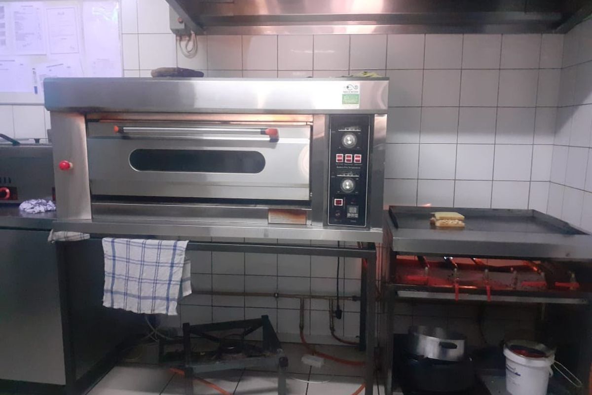 Commercial kitchen area featuring a built-in industrial oven, stainless steel extractor hood, and flat-top grill with tiled wall splashbacks.