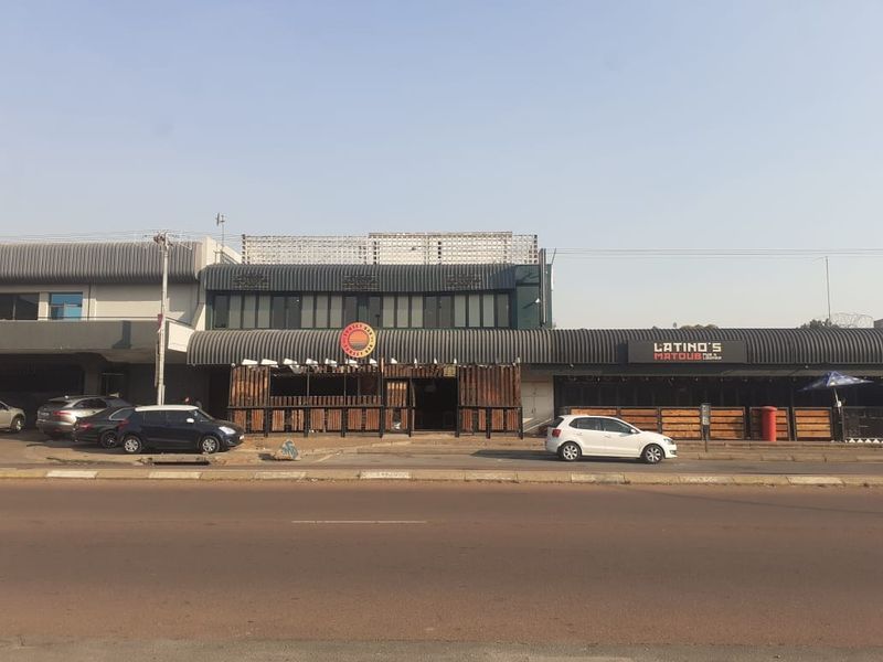 Street-level view of a commercial property featuring a multi-unit facade with integrated signage, metal roofing, and timber-clad outdoor seating areas.