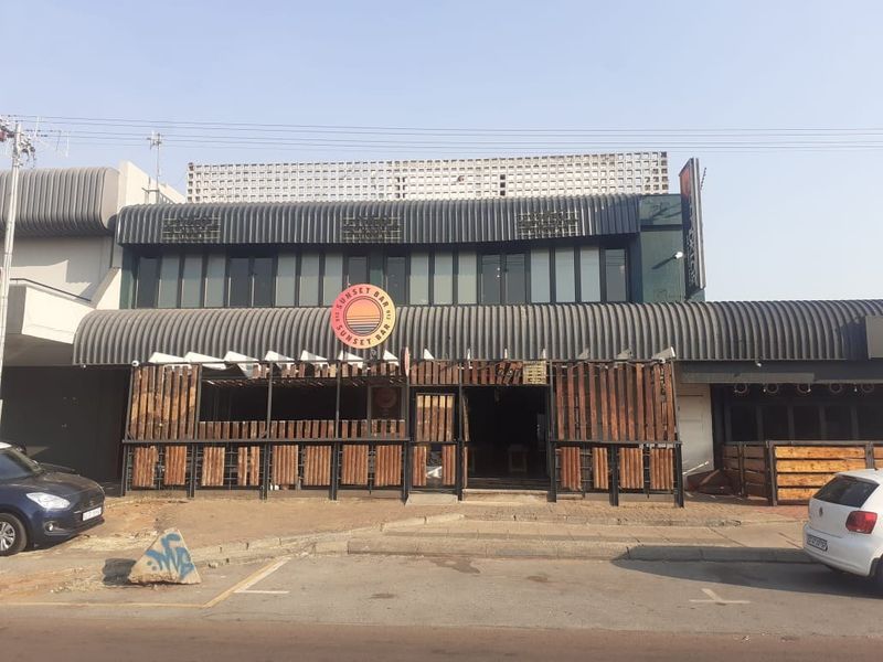 Commercial property exterior featuring a prominent Sunset Bar sign, corrugated metal roofing, and timber-slatted facade elements at the street-level entrance.