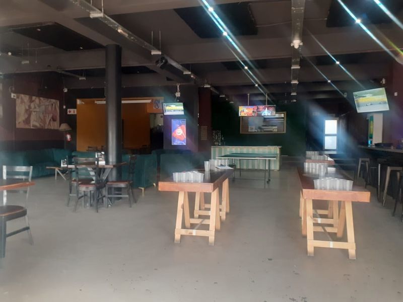 Spacious commercial open-plan area featuring exposed ceiling infrastructure, industrial-style lighting, and a built-in bar counter, suitable for a restaurant or entertainment venue.