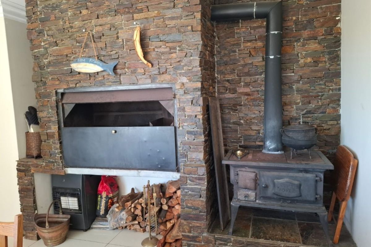Indoor entertainment area featuring a large stone-clad fireplace with a built-in braai and a cast-iron wood-burning stove.