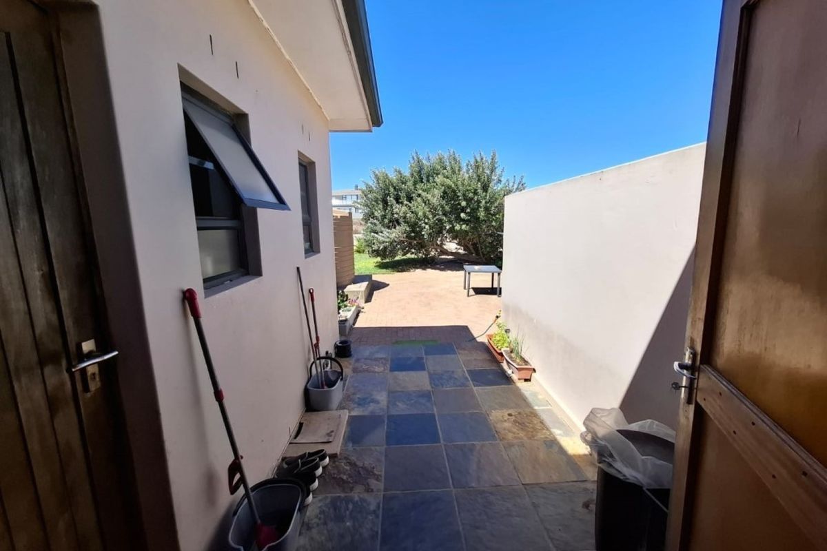 A paved outdoor walkway leading from a side entrance to a rear garden area, featuring stone tile flooring and boundary walls.