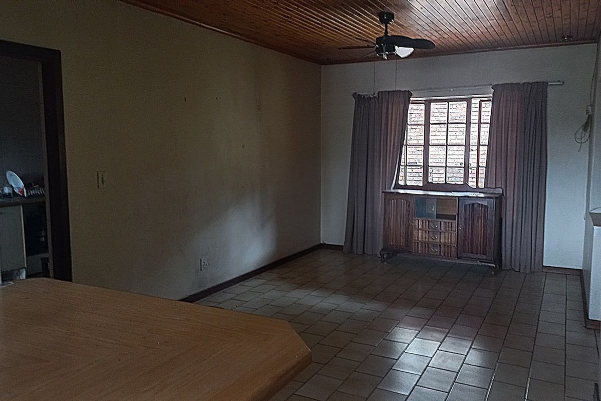 A living area featuring tiled flooring, a timber-paneled ceiling with a fan, and a window with curtains.
