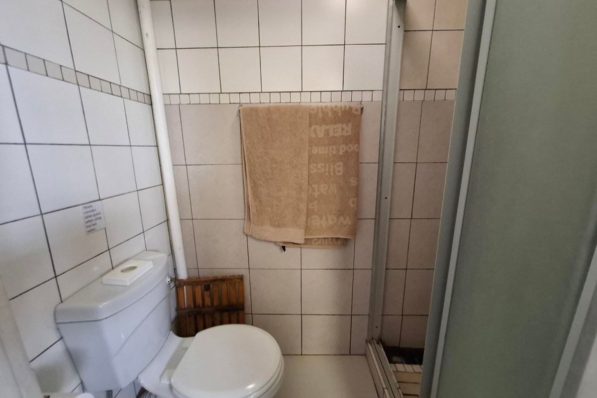 A compact bathroom featuring a standard toilet and a shower enclosure with tiled walls and dated finishes.