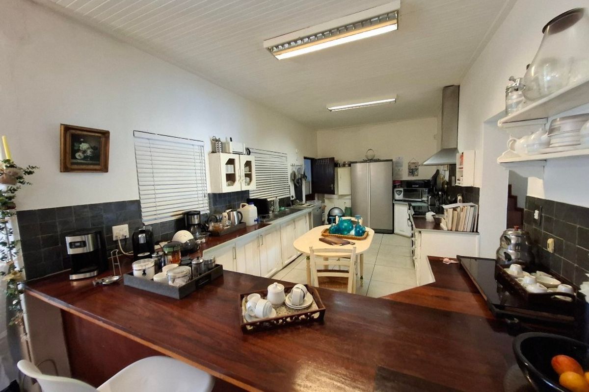 A functional kitchen featuring a long wooden breakfast bar, white cabinetry, tiled backsplash, and integrated stainless steel extractor fan.