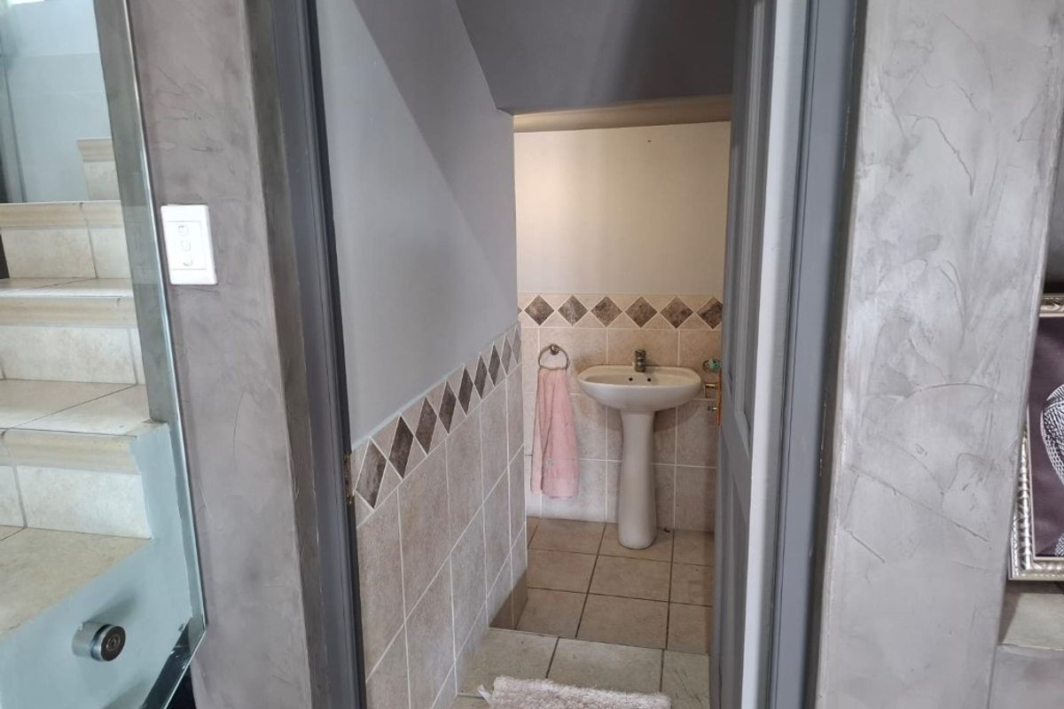 A compact guest bathroom featuring a pedestal basin, tiled flooring, and decorative wall tiling.