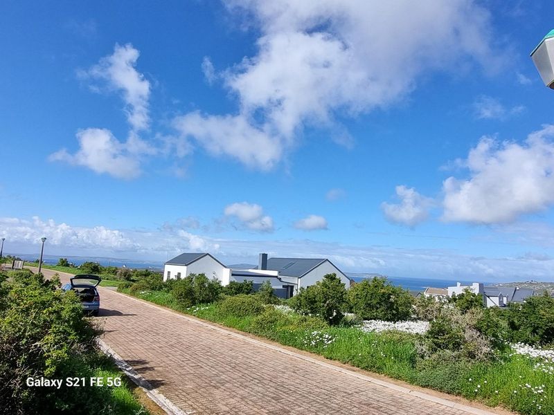 A street-level view of the property showing the paved driveway, modern pitched roof architecture, and surrounding coastal landscape.