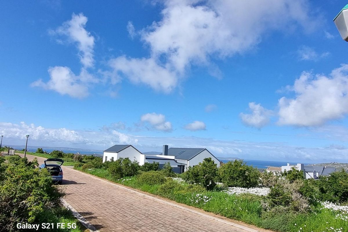 A street-level view of the property showing the paved driveway, modern pitched roof architecture, and surrounding coastal landscape.