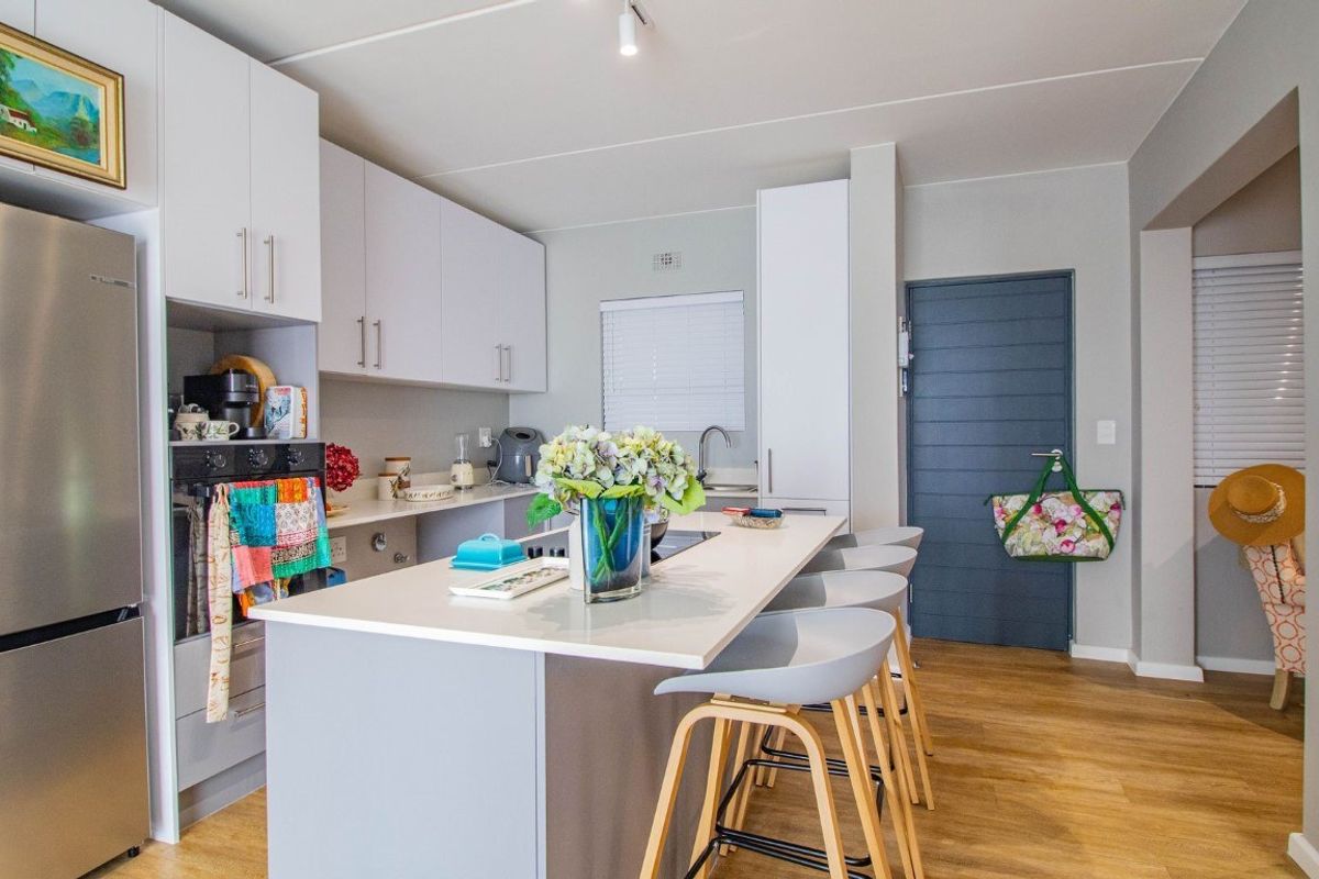 Modern kitchen featuring white cabinetry, stone countertops, a central island with breakfast bar seating, and wood-look flooring.