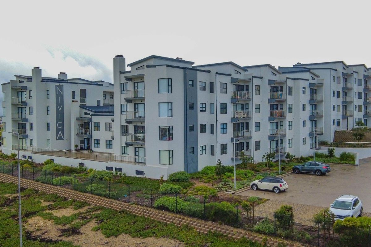 Aerial view of the Nivica apartment complex, showcasing the modern multi-story building architecture, surrounding landscaped grounds, and paved parking area.