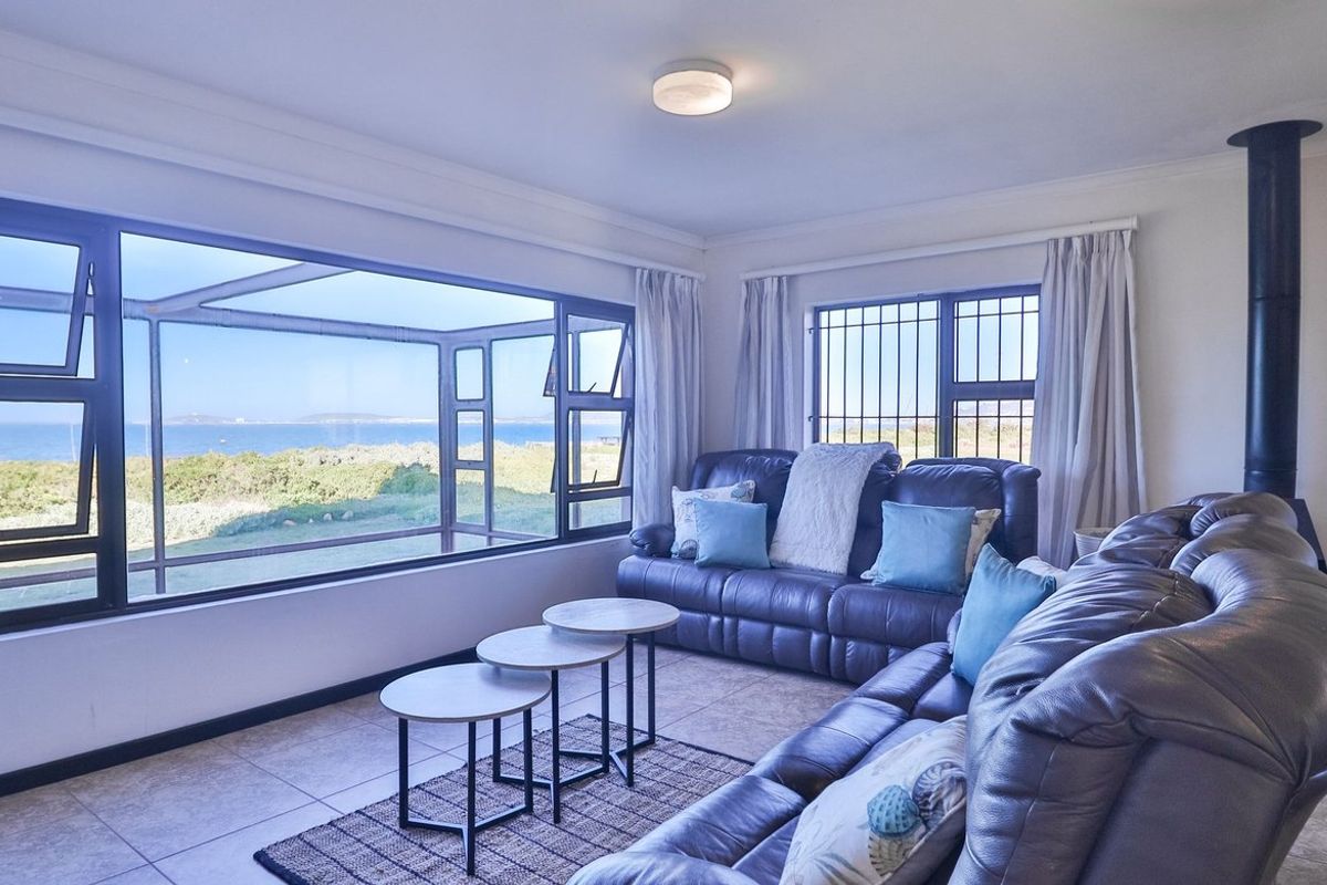 Bright living room featuring large picture windows with scenic coastal views, tiled flooring, and a modern freestanding fireplace.
