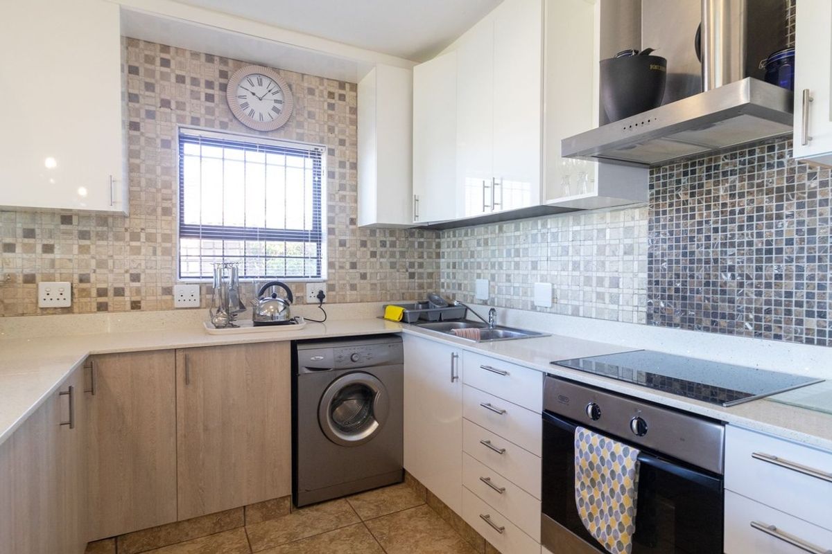 Modern kitchen featuring white and wood-tone cabinetry, stone countertops, mosaic tile backsplash, and integrated stainless steel appliances including an oven and extractor fan.