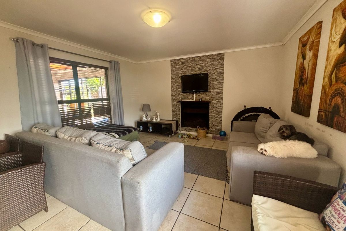 A comfortable living room featuring tiled flooring and a stone-cladded fireplace feature wall with direct access to the patio.
