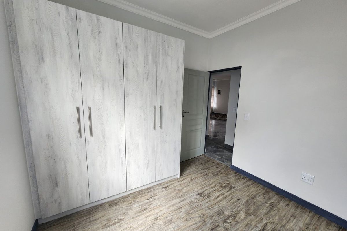 A clean bedroom featuring light wood-look flooring, built-in wardrobes with a modern finish, and crown molding.
