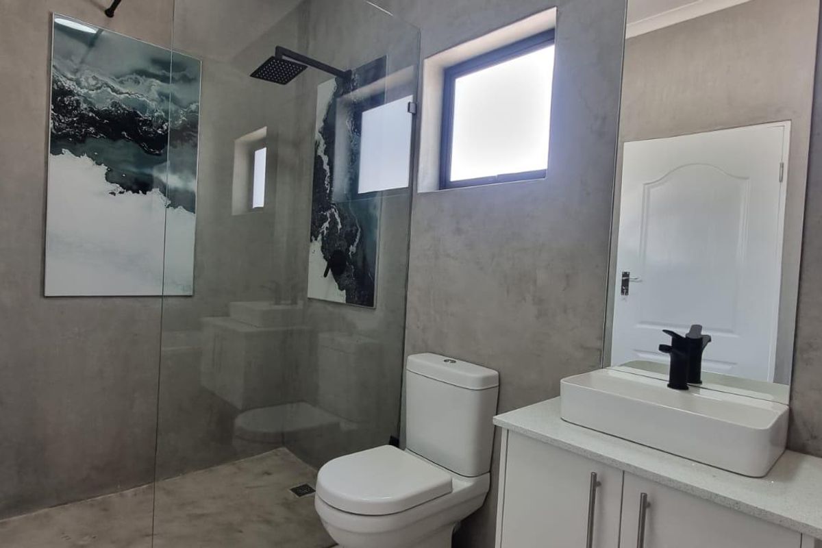 Modern bathroom featuring a walk-in shower with a rain shower head, sleek black tapware, a vanity with a countertop basin, and contemporary cement-look walls.