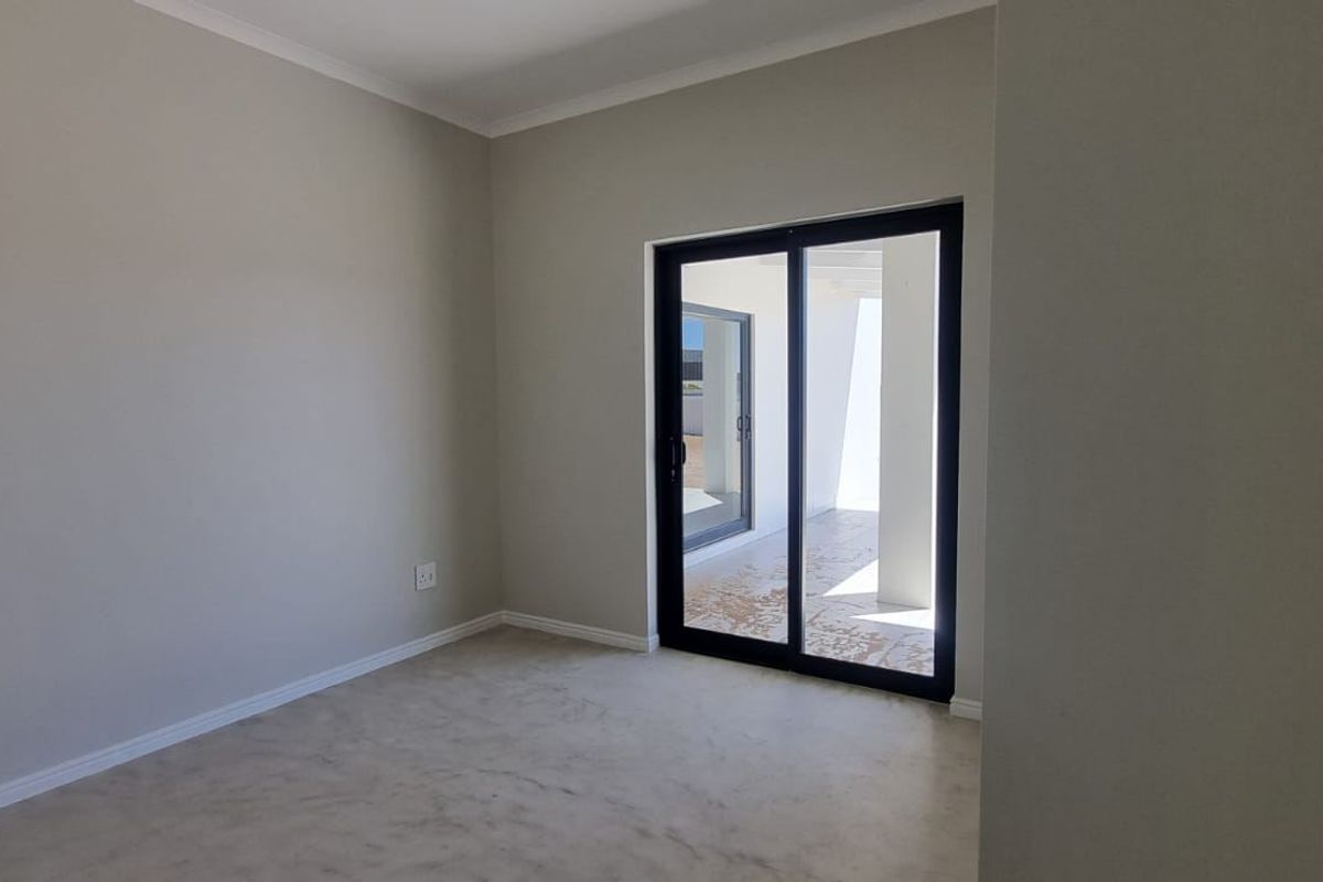 A bright, empty bedroom featuring neutral walls, smooth flooring, and a sliding glass door providing access to an outdoor patio area.