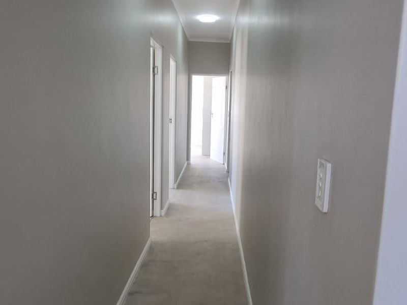A long, empty hallway featuring neutral wall paint, recessed ceiling lighting, and multiple internal door access points.