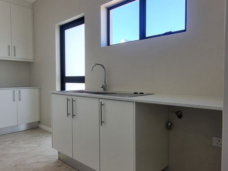 A clean, modern scullery featuring white built-in cabinetry, stone countertops, a stainless steel sink, and dedicated plumbing connections for appliances.