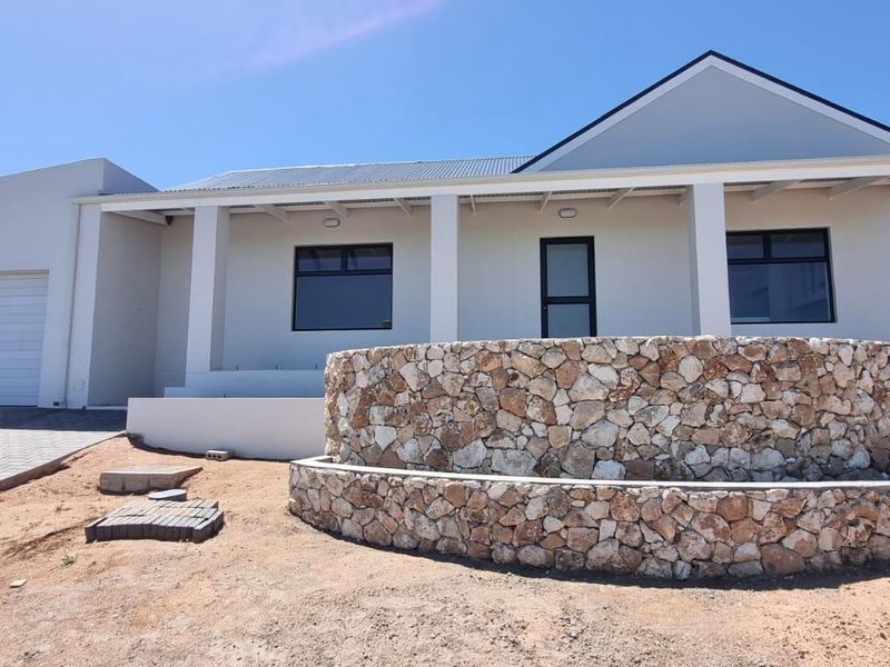 Front elevation of a modern house featuring a stone-clad feature wall, paved driveway, attached garage, and a covered entrance patio.